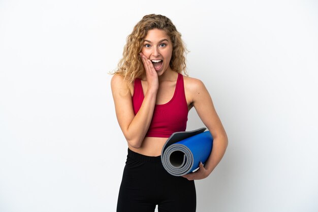 Young sport blonde woman going to yoga classes while holding a mat isolated on white background with surprise and shocked facial expression