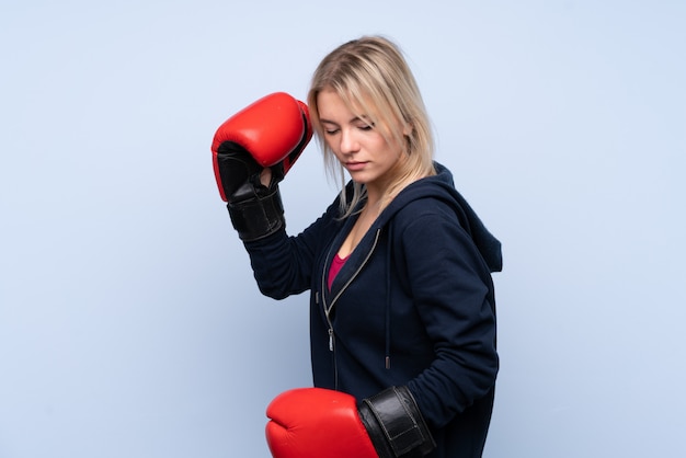 Photo young sport blonde woman over isolated blue wall with boxing gloves