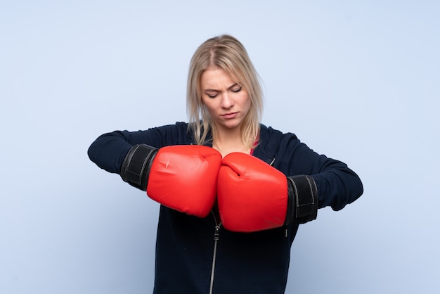 Young sport blonde woman over isolated blue wall with boxing gloves