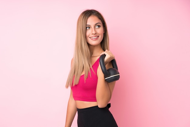 Young sport blonde woman over isolated pink  making weightlifting