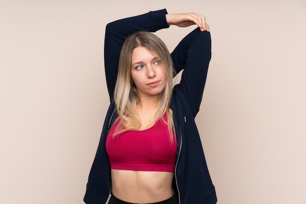 Young sport blonde woman over isolated wall stretching