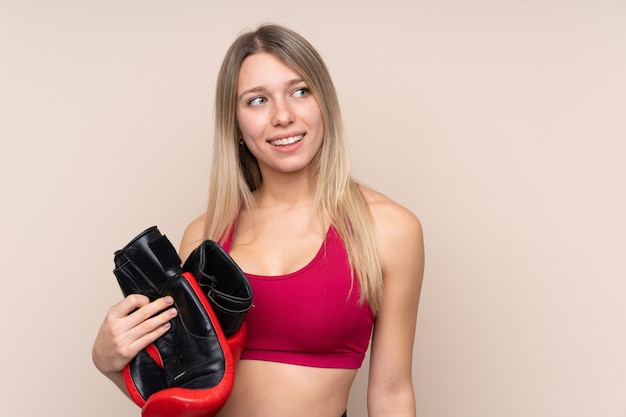 Молодая спортивная блондинка над изолированной стеной с боксерскими перчатками