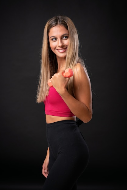 Young sport blonde woman making weightlifting over isolated black background