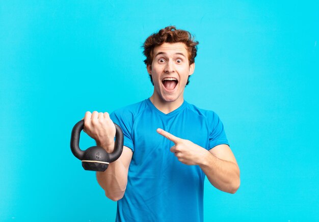 Young sport boy looking excited and surprised pointing to the side and upwards to copy space. dumbbell concept