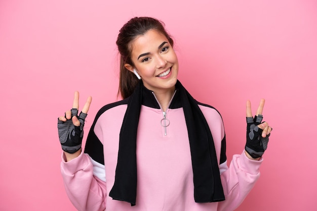 Young sport Brazilian woman isolated on pink background showing victory sign with both hands