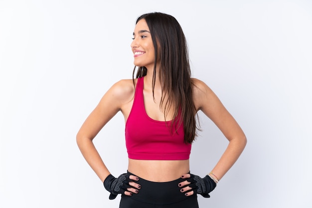 Foto giovane donna castana di sport sopra la parete bianca isolata che posa con le armi all'anca e che guarda lato