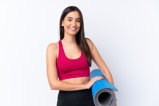 Young sport brunette woman over isolated white wall with a mat and smiling