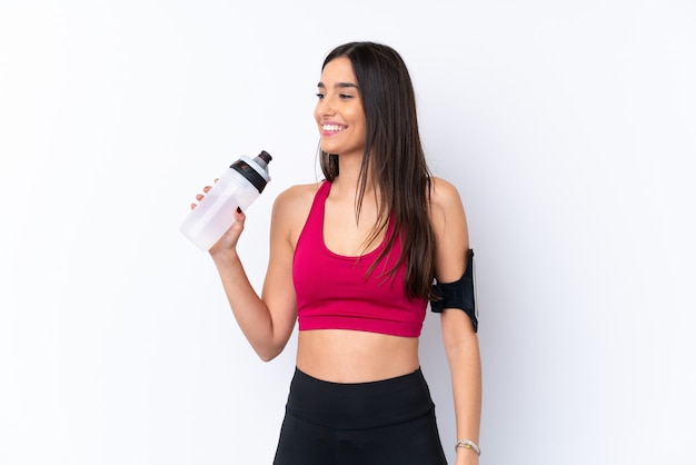Young sport brunette woman over isolated white wall with sports water bottle