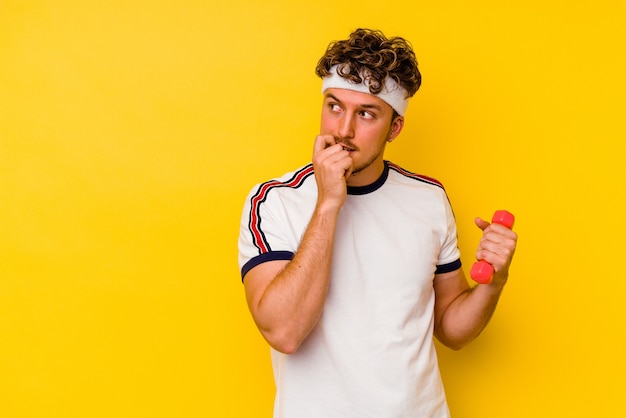 Young sport caucasian man holding a dumbbell isolated on a yellow background relaxed thinking about something looking at a copy space.