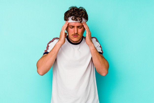 Young sport caucasian man isolated on blue background touching temples and having headache.