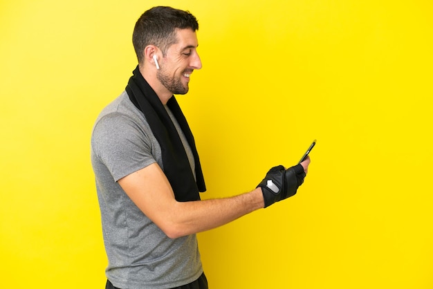 Young sport caucasian man isolated on yellow background keeping a conversation with the mobile phone with someone