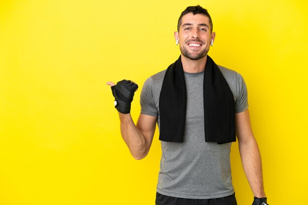 Young sport caucasian man isolated on yellow background pointing to the side to present a product