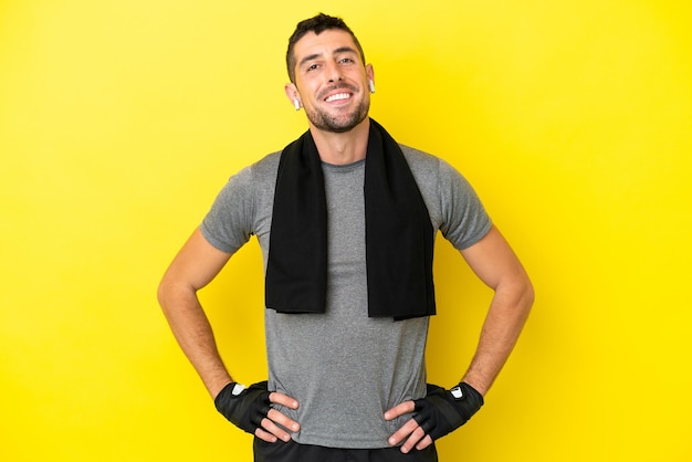 Young sport caucasian man isolated on yellow background posing with arms at hip and smiling