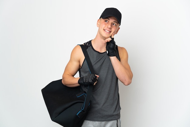 Young sport caucasian man with bag isolated on white wall thinking an idea while looking up