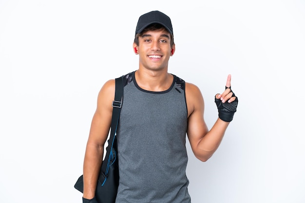 Молодой спортивный кавказец со спортивной сумкой на белом фоне показывает и поднимает палец в знак лучшего