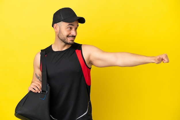 Young sport caucasian man with sport bag isolated on yellow background giving a thumbs up gesture