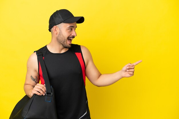 Young sport caucasian man with sport bag isolated on yellow background pointing finger to the side and presenting a product