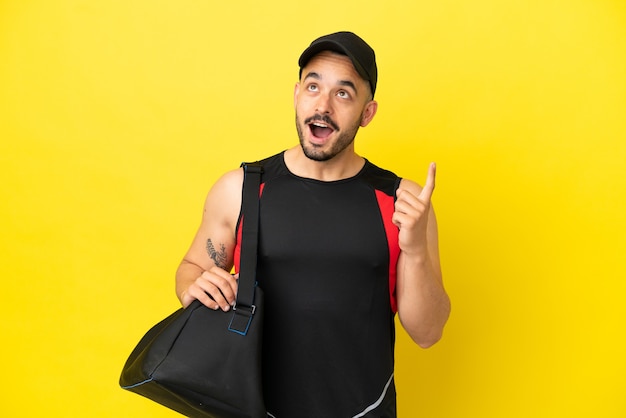 Young sport caucasian man with sport bag isolated on yellow background thinking an idea pointing the finger up