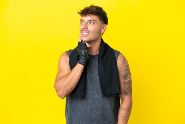 Young sport caucasian man with towel isolated on yellow background thinking an idea while looking up