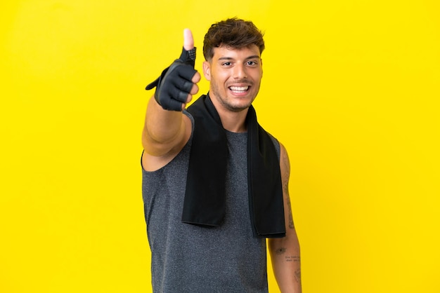 Young sport caucasian man with towel isolated on yellow background with thumbs up because something good has happened