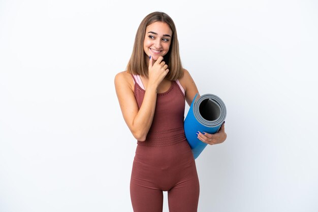 Young sport caucasian woman going to yoga classes isolated on white background looking to the side and smiling