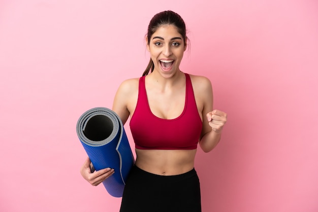 Young sport caucasian woman going to yoga classes while holding a mat celebrating a victory in winner position