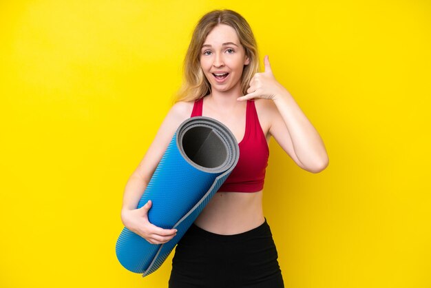 Young sport caucasian woman going to yoga classes while holding a mat isolated on yellow background making phone gesture call me back sign