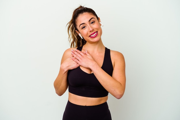 Young sport caucasian woman isolated on white background has friendly expression, pressing palm to chest. Love concept.