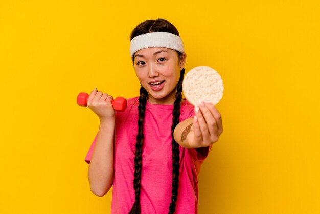 Young sport chinese woman eating rice cakes isolated on yellow background