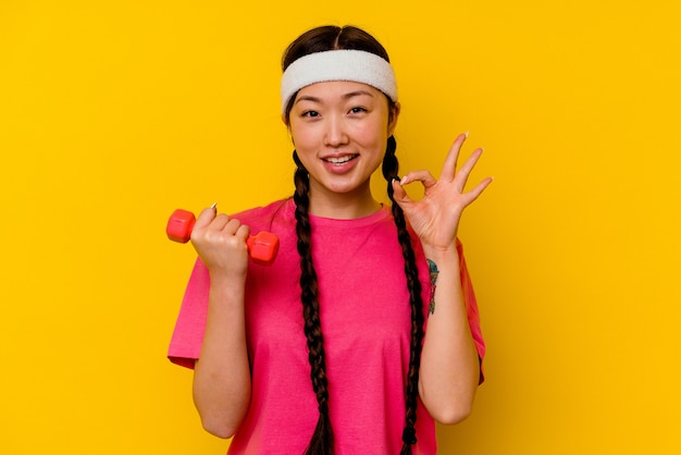 Young sport chinese woman isolated on yellow background cheerful and confident showing ok gesture.