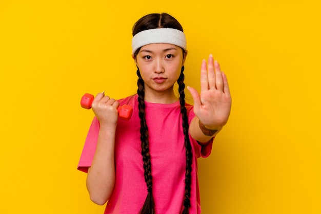 젊은 스포츠 중국 여자는 당신을 방지, 정지 신호를 보여주는 뻗은 손으로 서 노란색 배경에 고립.