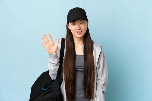 Young sport Chinese  woman with sport bag over isolated blue counting five with fingers