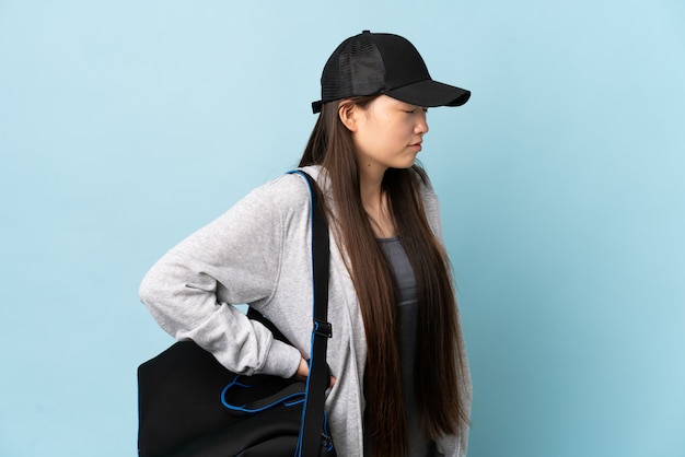 Foto giovane donna sportiva cinese con borsa sportiva su blu isolato sofferenza da mal di schiena per aver fatto uno sforzo