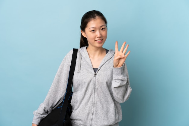 Young sport Chinese  woman with sport bag over isolated blue wall happy and counting four with fingers