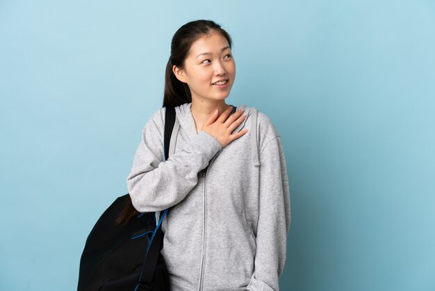 Young sport Chinese  woman with sport bag over isolated blue wall looking up while smiling