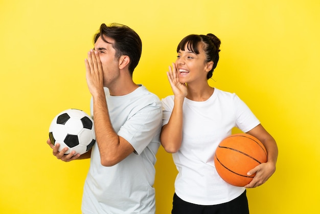 Young sport couple playing football and basketball isolated on yellow background shouting with mouth wide open to the lateral