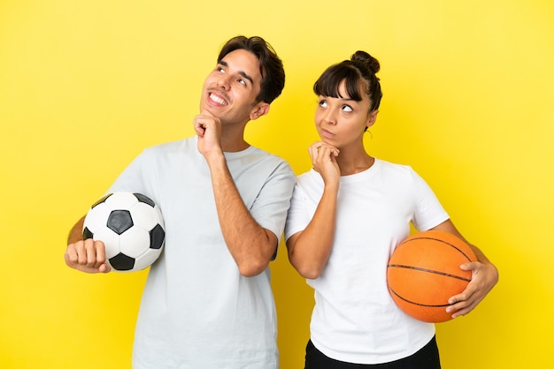 Young sport couple playing football and basketball isolated on\
yellow background thinking an idea while looking up