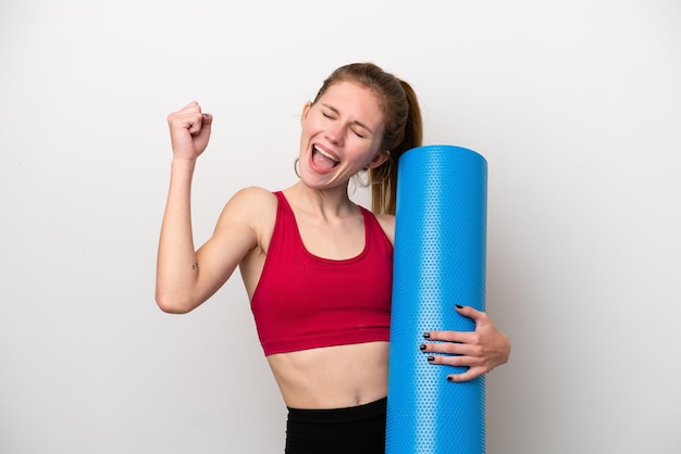 Young sport English woman going to yoga classes while holding a mat isolated on white background celebrating a victory