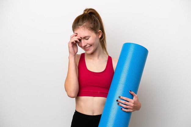 Young sport English woman going to yoga classes while holding a mat isolated on white background laughing