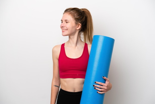 Young sport English woman going to yoga classes while holding a mat isolated on white background looking side