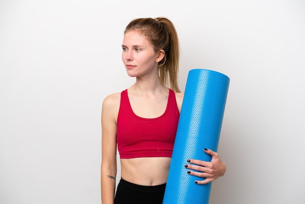 Young sport English woman going to yoga classes while holding a mat isolated on white background looking to the side