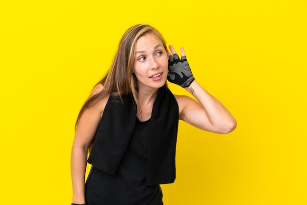 Young sport English woman isolated on white background listening to something by putting hand on the ear