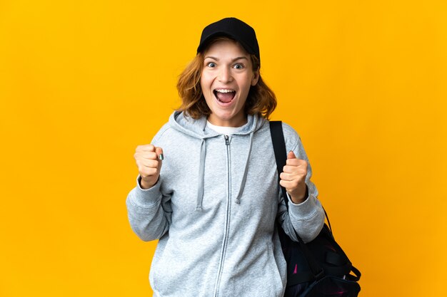 Young sport Georgian woman with sport bag over isolated wall celebrating a victory in winner position