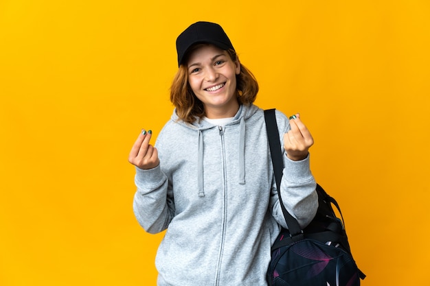 Молодая спортивная грузинка со спортивной сумкой над изолированной стеной делает денежный жест