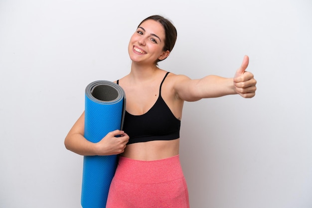 Young sport girl going to yoga classes while holding a mat isolated on white background giving a thumbs up gesture