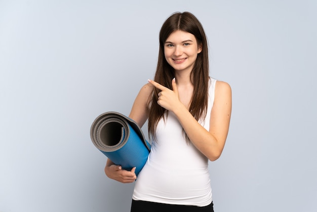 Young  sport girl going to yoga classes while holding a mat pointing to the side to present a product