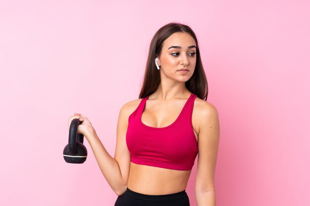 Young sport girl over isolated pink  making weightlifting with kettlebell