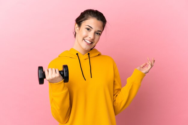 Young sport girl making weightlifting over isolated pink background extending hands to the side for inviting to come