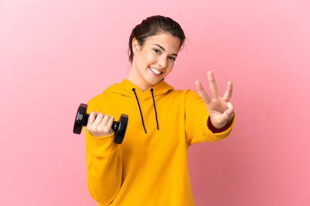 Young sport girl making weightlifting over isolated pink background happy and counting three with fingers