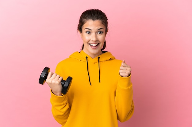 Young sport girl making weightlifting over isolated pink wall celebrating a victory in winner position